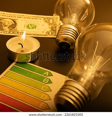 Electric lamp and candle on a dark background. Incandescent lamp, 1 dollar usa and a candle. Shutdown or blackout of electricity. High electricity prices. Saving electricity.