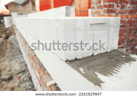 Laying autoclaved aerated concrete blocks with reinforcement and adhesive. Installing white blocks close up. Masonry. Process of house building at construction site Royalty-Free Stock Photo #2261829847