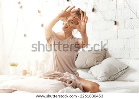 Young woman  makes gesture heart with fingers. Concept of  love. Bright home interior.
