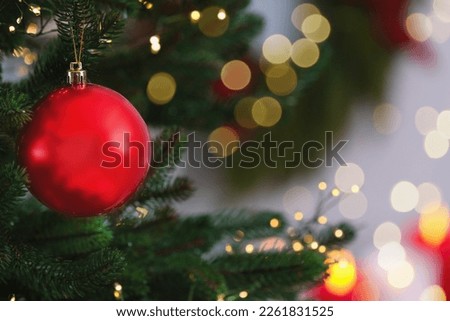 Beautiful Christmas ball hanging on fir tree branch against blurred background, closeup. Space for text