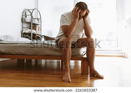 concept of life-weary, suffering, sick man. middle-aged man suffering from insomnia, depression, sits on bed with head down and covers face with hands. Royalty-Free Stock Photo #2261833387