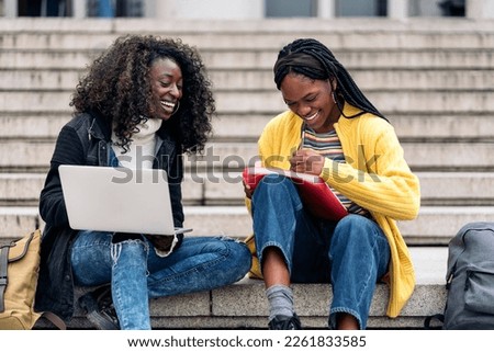 Stock photo of black friends using laptop while sitting in stairs and doing homework.