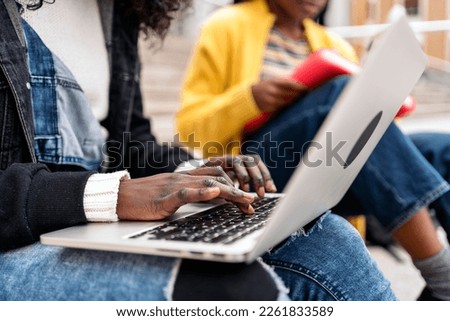 Stock photo of unrecognized black woman using laptop while sitting in stairs.