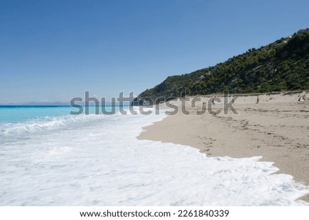 Sunny sandy beach, waves and beautiful turquoise blue sea and rocks. Milos beach, Lefkada island, Greece.