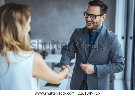 Business people shaking hands after successful meeting. Businessman And Businesswoman Shaking Hands In Office. Businessman shaking hands with his female partner celebrating successful teamwork. Royalty-Free Stock Photo #2261849919