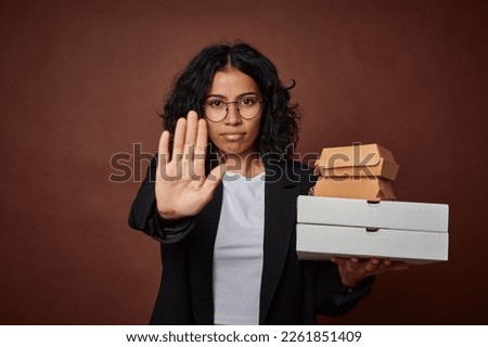 Young business woman holding a fast food pack standing with outstretched hand showing stop sign, preventing you.