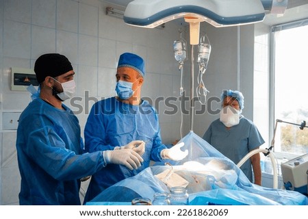 VINNITSA,UKRAINE .OCTOBER 25 of 2022:A horizontal skilled surgeons and a watchful nurse performing an operation under the bright electric lamp in a modern operation center in  hospital in Vinnitsa.