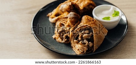 Crepes stuffed with chicken and mushrooms with sour cream on the wooden table. Banner for website