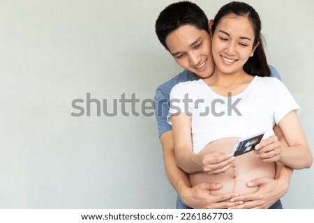 Young happy asian future parents holding and watching with emotion sonography pictures of their first baby. Young couple expecting and exciting a baby. New Parenting concept.