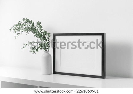 Black horizontal frame mockup in white room with fresh eucalyptus plant in vase