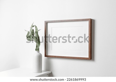 Wooden frame mockup on white wall with copy space for artwork, photo or print presentation in minimalistic interior with dry eucalyptus