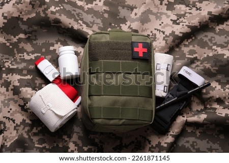 First aid kit with medical tourniquet, pills and bands on military fabric, flat lay