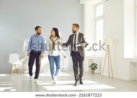 People and real estate. Young married couple in love together inspects house shown to them by male realtor. Real estate agent talks about benefits of house to family who walks by him holding hands. Royalty-Free Stock Photo #2261877223