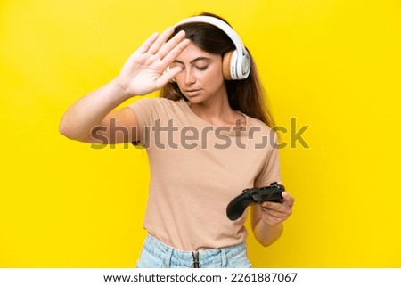 Young caucasian woman playing with a video game controller isolated on yellow background making stop gesture and disappointed