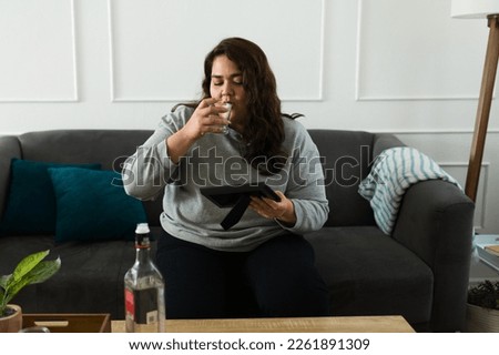 Heartbroken sad woman looking at a picture frame of her ex-boyfriend while drinking alcohol and missing him after a breakup