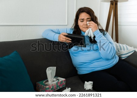 Obese woman crying wiping her tears with tissues because of her sad heartbroken breakup looking at the picture frame