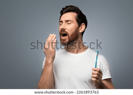 Middle aged man holding hand near mouth and checking breath freshness, worrying about poor oral hygiene, suffering from unpleasant odor, standing over grey background Royalty-Free Stock Photo #2261893763