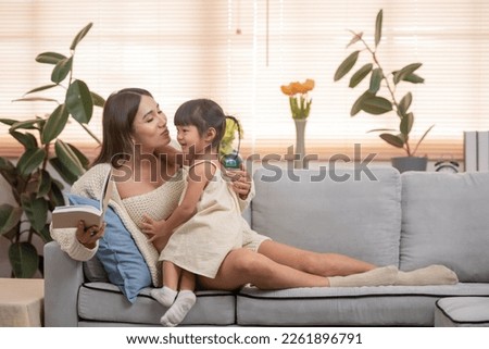 young pregnant mother reading book to her toddler daughter at home,
Image of attractive family pregnant woman and her little daughter smiling and reading book while sitting on sofa at home.