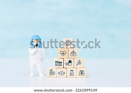 Miniature doctor wearing protection suit with medical icon cube on blue background, health care and medical concept, doctor in PPE suit to protect against coronavirus covid-19