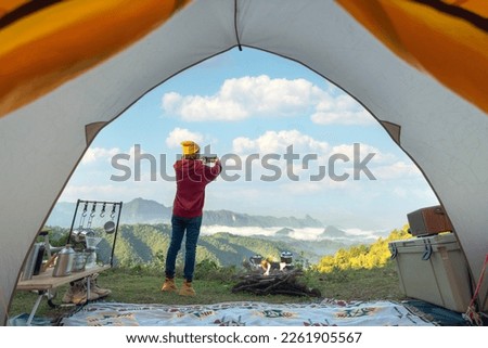 Woman traveller take a photo by her smartphone for keep a mountain view in front of her tent in camping