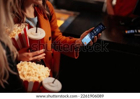 A young adult woman is checking the seats for the movie projection in the theater on her mobile app. Royalty-Free Stock Photo #2261906089