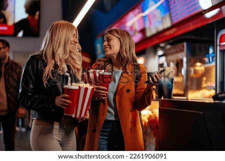 Two young joyful Caucasian girlfriends are in a movie theater with their beverages and popcorns on their way to see a movie in the theater. Royalty-Free Stock Photo #2261906091