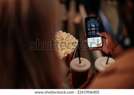Two young people are in a movie theater purchasing movie tickets with an online mobile app. Royalty-Free Stock Photo #2261906405