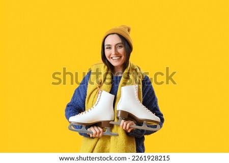Pretty young woman with ice skates on yellow background