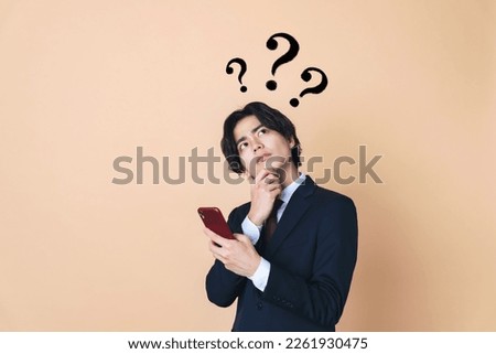 Thoughtful young Asian man with a smart phone. Royalty-Free Stock Photo #2261930475