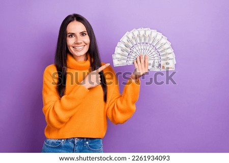 Photo of young cheerful satisfied business woman wear orange turtleneck direct finger dollars financial assistant isolated on violet color background