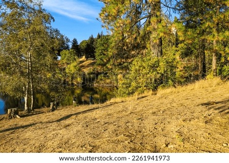 people fishing on the banks of the lake with lush green and autumn colored trees and blue sky at Lake Gregory in Crestline California	