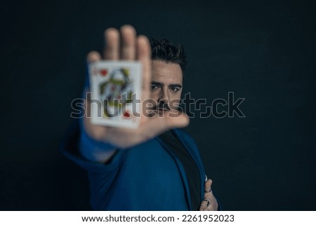 Blurred portrait of a young magician in the dark showing in the palm of his hand a hidden card while looking at the camera. His face is in focus.