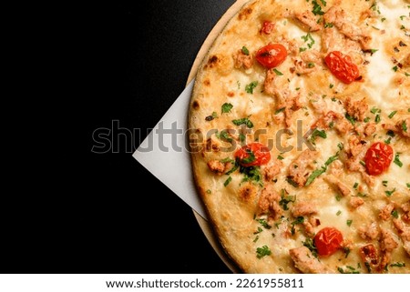 Great top view on fragment of delicious hot pizza with cherry tomatoes and chicken garnished by green on a black table. Copy space