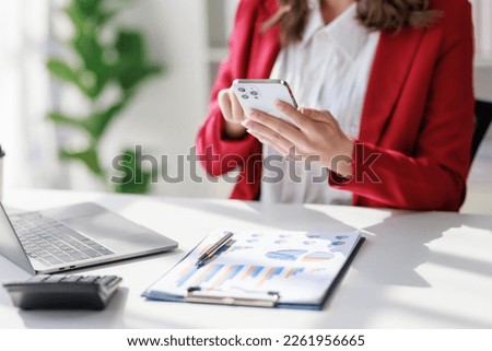 Concept of business investment or working woman,Close up businesswoman wearing red suit sitting while using smartphone working on business investment documents and  talk to client about business data.