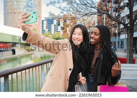 A couple of multiracial happy girls having fun takng a photo with a cellphone. Two young women smiling doing a selfie portrait with a smart phone in a shopping sale day. Lifestyle concept. High