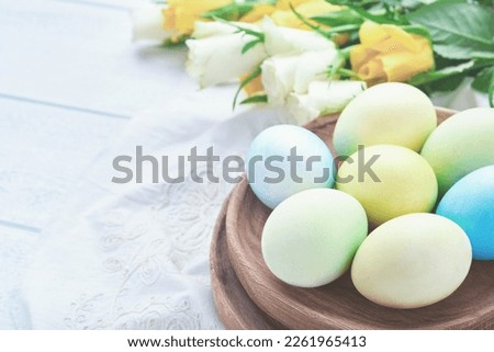 Happy Easter. Easter eggs on rustic table with white and yellow roses. Natural dyed colorful eggs in wooden plate and spring flowers in rustic room.  Toned image. Easter background with copy space.
