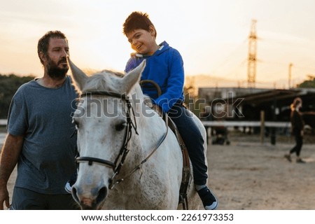 Physiotherapist working with a child with a disability in an equine therapy session. Royalty-Free Stock Photo #2261973353