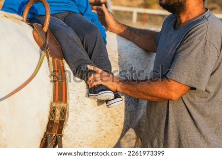 Equine therapy instructor helping a kid with disabilities on the horse. Royalty-Free Stock Photo #2261973399