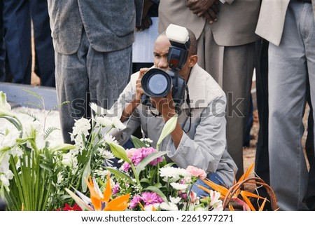 young african photographer taking pictures at a funeral over the flower on the grave