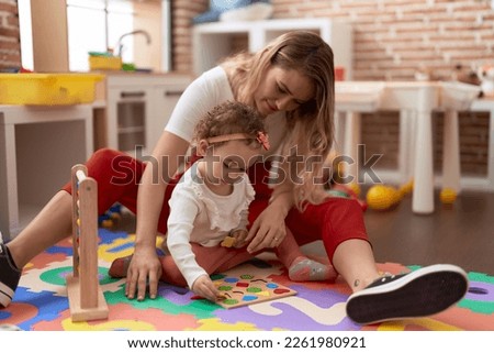 Teacher and toddler playing with maths puzzle game sitting on floor at kindergarten