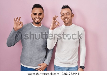Homosexual couple standing over pink background smiling positive doing ok sign with hand and fingers. successful expression. 