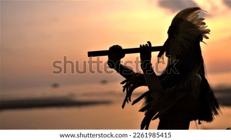 Silhouette of a Native American Indian playing a bamboo flute against a sunset background