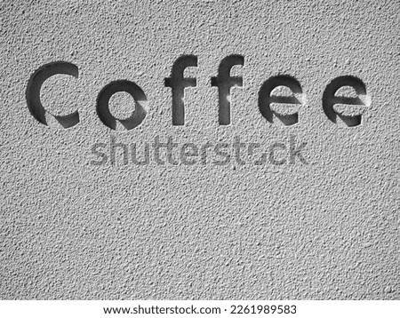 The word "Coffee", the letters carved into the words on the grunge concrete wall with copy space, vertical. Light and shadow in the carving font on the grey cement stone wall texture.
