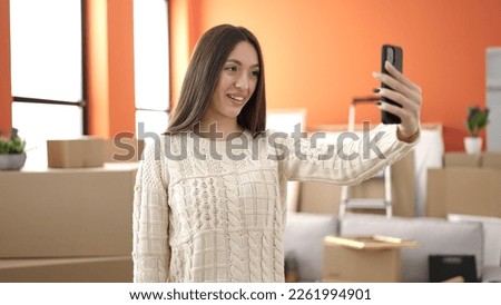 Young beautiful hispanic woman make selfie by smartphone standing at new home