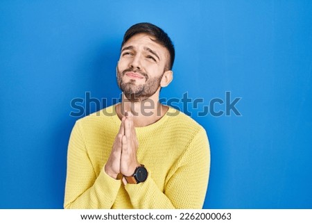 Hispanic man standing over blue background begging and praying with hands together with hope expression on face very emotional and worried. begging.  Royalty-Free Stock Photo #2262000063