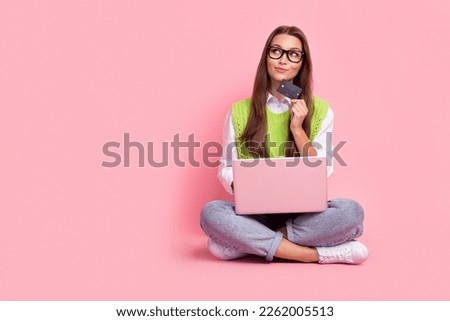 Full length photo of thoughtful smart girl straight hairdo green vest hold laptop card look empty space isolated on pink color background