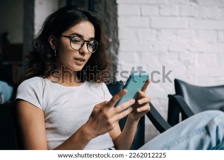 Caucasian female blogger in optical eyewear for vision protection using cellphone technology for social networking in social media, millennial woman with smartphone making online booking and banking