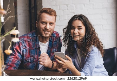 Portrait of Caucasian male and female with cellular gadget looking at camera during leisure time, millennial best friends with smartphone technology posing during date meeting in cafe interior Royalty-Free Stock Photo #2262012969