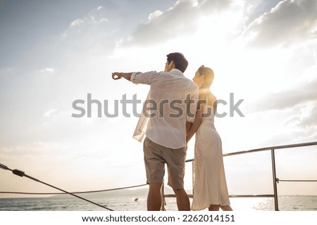Asian young romantic couple looking at beautiful view during yachting. Attractive man and woman hanging out celebrating anniversary honeymoon trip while catamaran boat sailing during summer sunset. Royalty-Free Stock Photo #2262014151