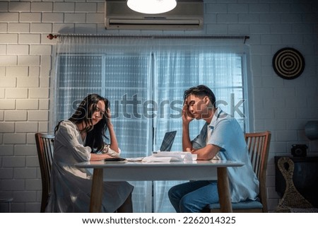 Asian young depressed couple having argument while checking money debt. Attractive new marriage man and woman looking frustrated to paperwork and bill, feel worried about financial problem in house.